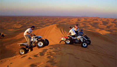 Two riders on ATVs on golden sand dunes in desert landscape at dusk, Jeddah